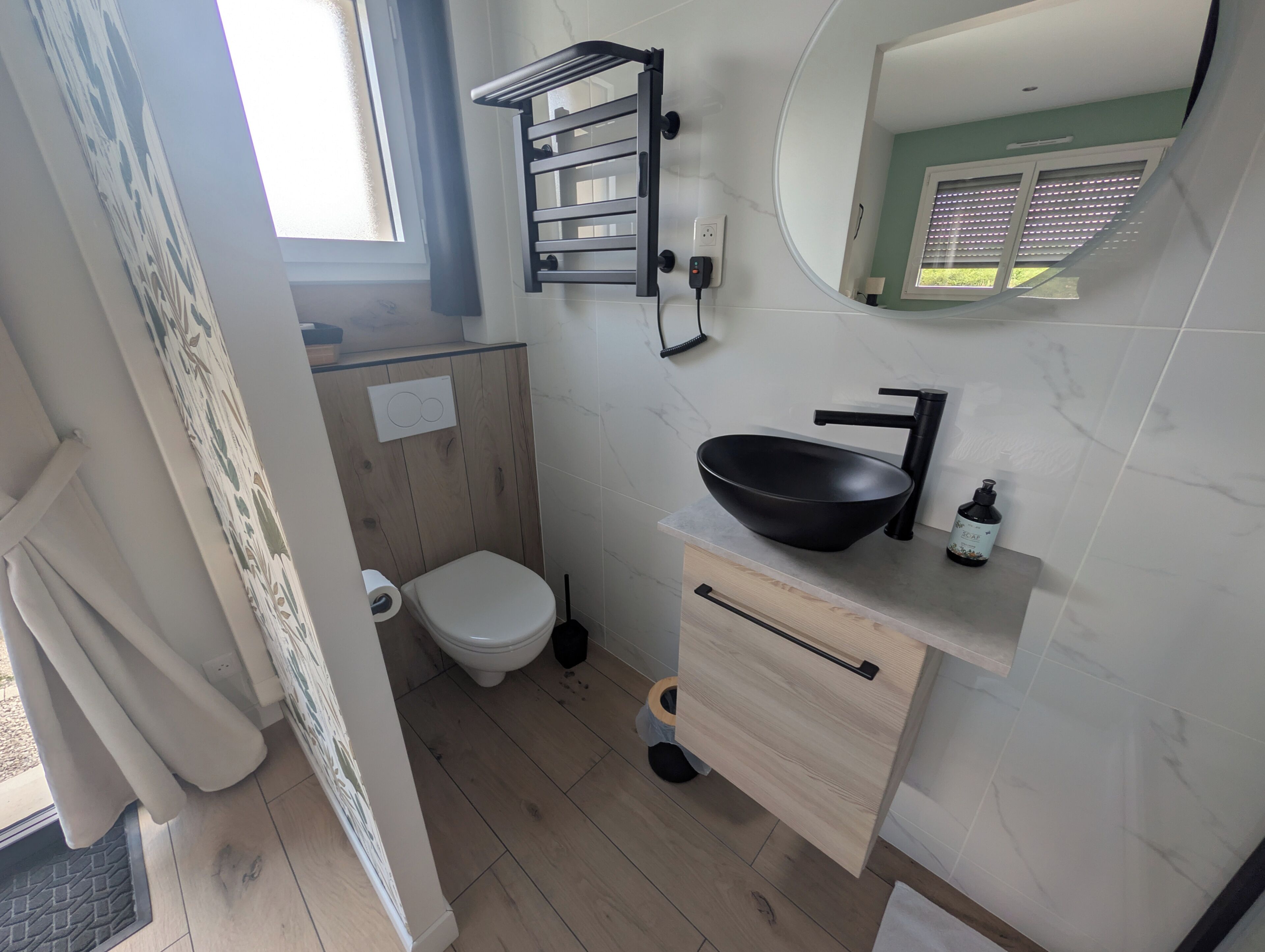 A bathroom with a toilet, a black vessel sink, a mirror, and a window.