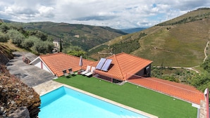 Una piscina con un edificio de techo rojo, un césped verde y un paisaje montañoso al fondo.