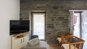 Una habitación con pared de piedra, un televisor en un mueble, un sofá y sillones de mimbre.