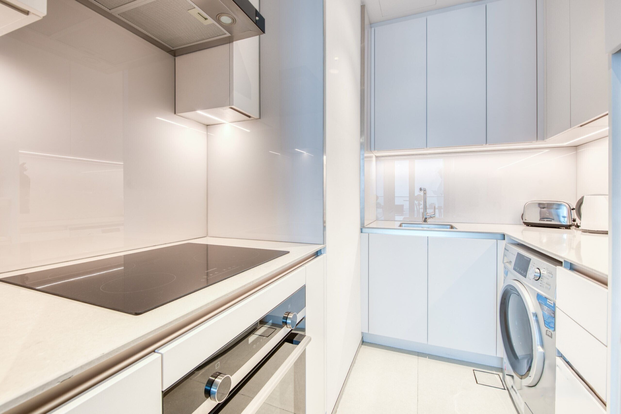 Een moderne keuken met een inbouwfornuis, oven, magnetron en een wasmachine.