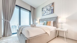 Ein modernes Hotelzimmer mit einem großen Bett, Blick auf die Stadt, einem Bild an der Wand und einer Nachttischlampe.