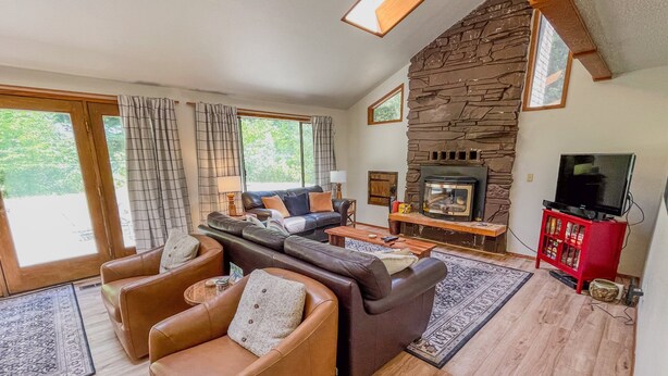 A living room with leather sofas, a fireplace, a TV, and a stone wall. - Wilderness Edge | Hot Tub, Wifi, Fireplace (Packwood)