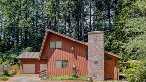 A two-story building with a garage, a brick chimney, and a wooden deck. - Wilderness Edge | Hot Tub, Wifi, Fireplace (Packwood)