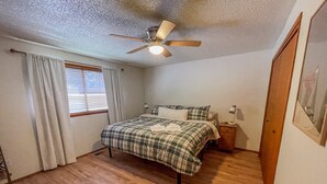 A bedroom with a bed, a ceiling fan, a window with curtains, a nightstand, and a framed picture on the wall. - Wilderness Edge | Hot Tub, Wifi, Fireplace (Packwood)