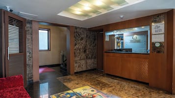 Un vestíbulo de hotel con una recepción, una silla roja y un suelo de mármol.