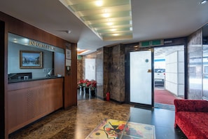 Un área de recepción con piso de mármol, mostrador de recepción, sofá rojo y puerta de cristal que da al exterior.