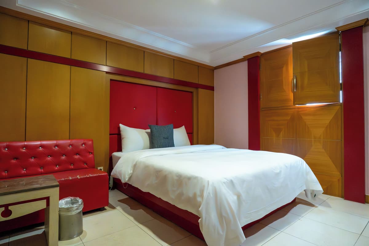 A hotel room with a red upholstered sofa, a bed with white bedding, and a wooden wardrobe.