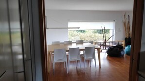 A modern dining area with a wooden table and white chairs, a large window with a view, and a black bean bag on the floor. - House with a private pool, Caminha (Viana do Castelo)