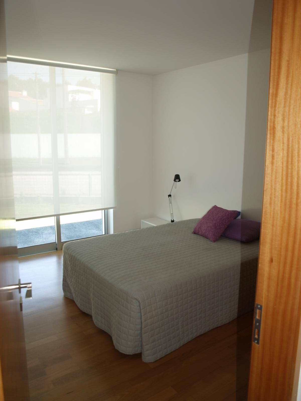 Quarto com cama, mesa de cabeceira, luminária e janela com persianas.