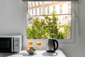 Eine Küche mit Mikrowelle, einer Schale Gebäck, zwei Orangensaftgläsern und einer Kaffeemaschine an einem Fenster mit Blick auf Gebäude und Grünflächen.
