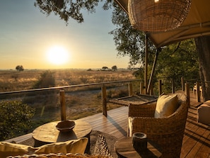 A wooden deck with wicker furniture, a table, and a hanging basket. - Thitaka River Lodge by NEWMARK (Kongola)