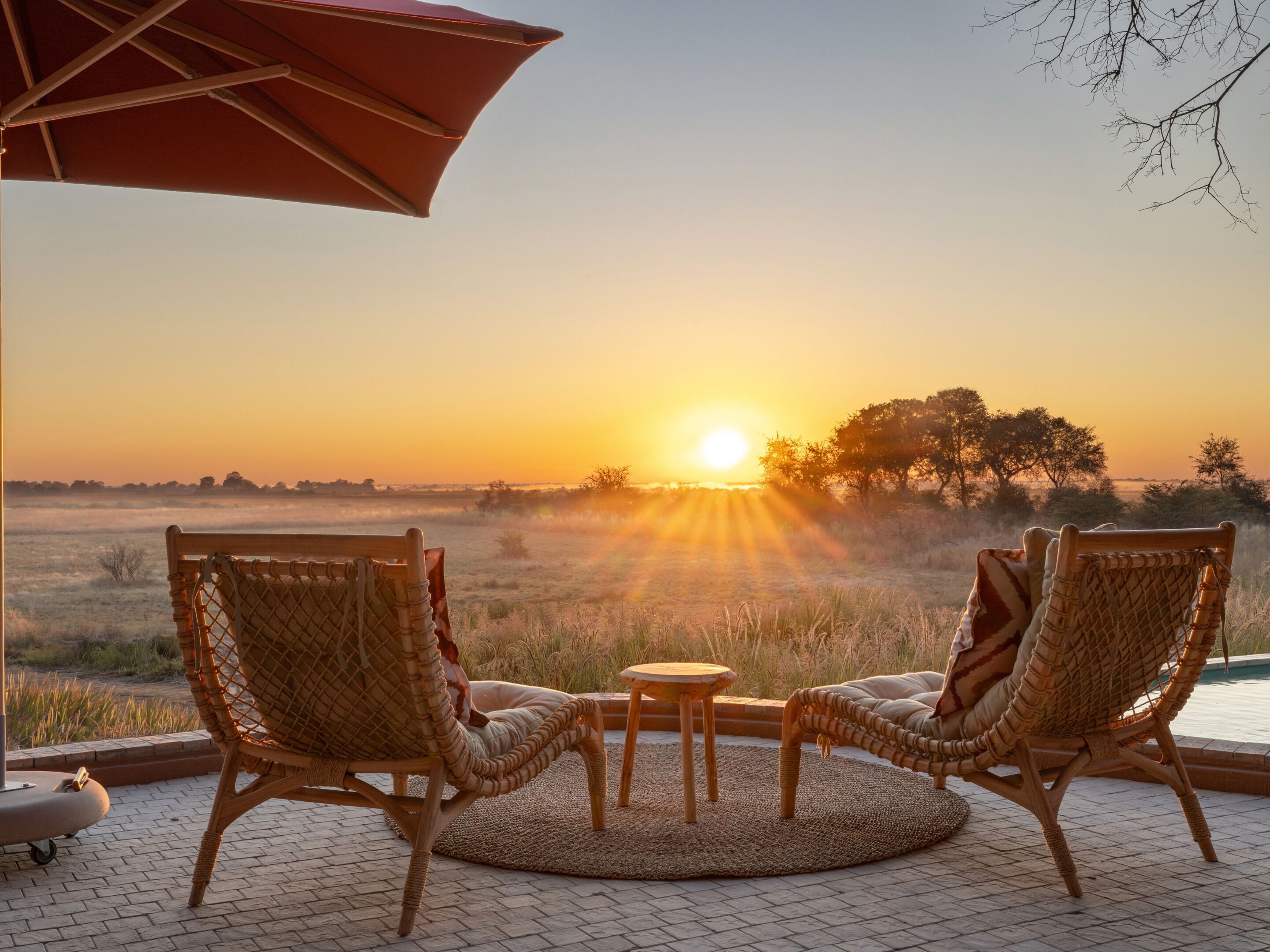 A wicker chair and table set on a patio with a view of the sunset over a field.