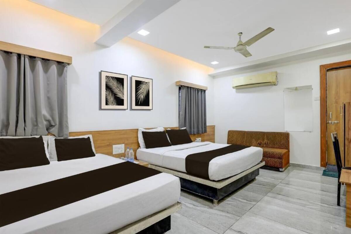 Quarto de hotel com duas camas, um ventilador de teto, um aparelho de ar condicionado e uma porta de madeira.