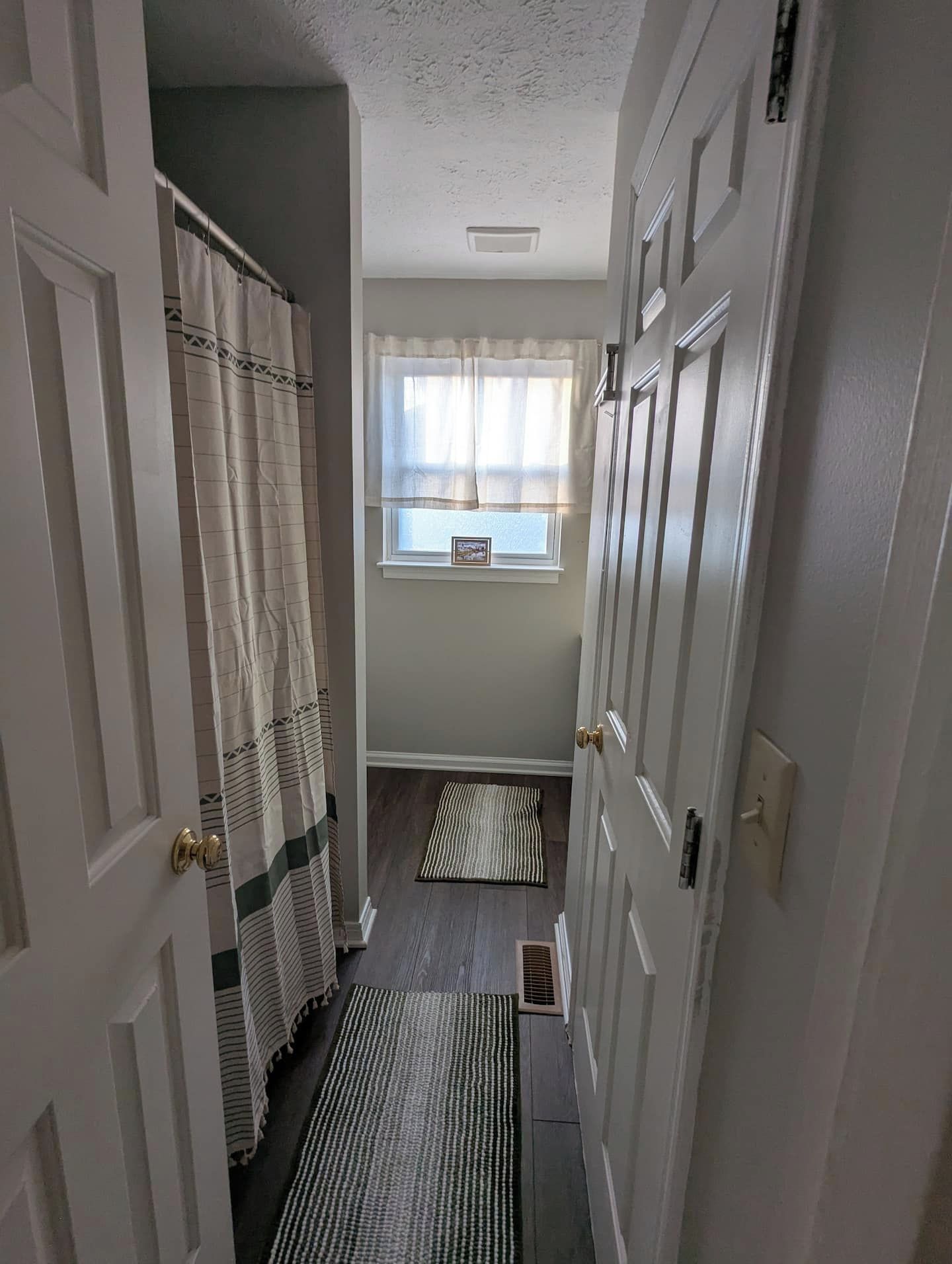 Un couloir étroit avec une fenêtre, une porte et un espace douche.