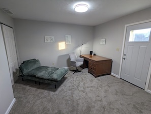Huoneessa on sänky, työpöytä ja tuoli. Siinä on kaksi ovea, yksi kummallakin puolella huonetta.
