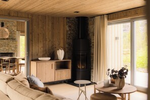 A cozy living room with a stone fireplace, wooden furniture, and a large window.