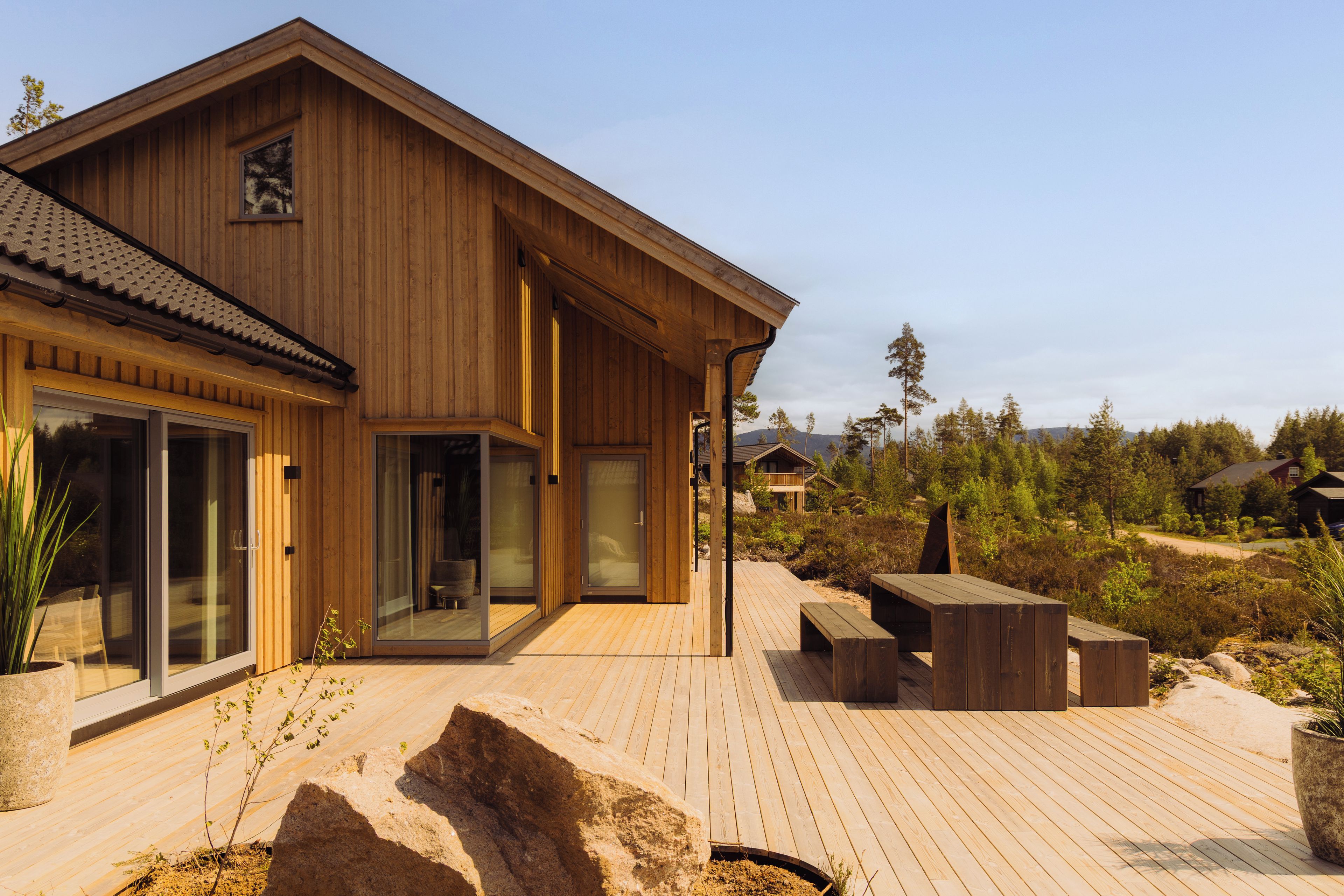 A wooden house with a deck, large sliding glass doors, and a view of the surrounding landscape.