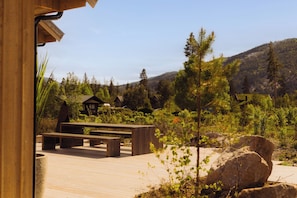 Une terrasse en bois avec des bancs, entourée de verdure et offrant une vue sur les montagnes en arrière-plan.