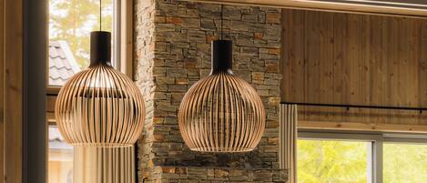A modern dining area with a stone fireplace, wooden ceiling, and two hanging pendant lights.