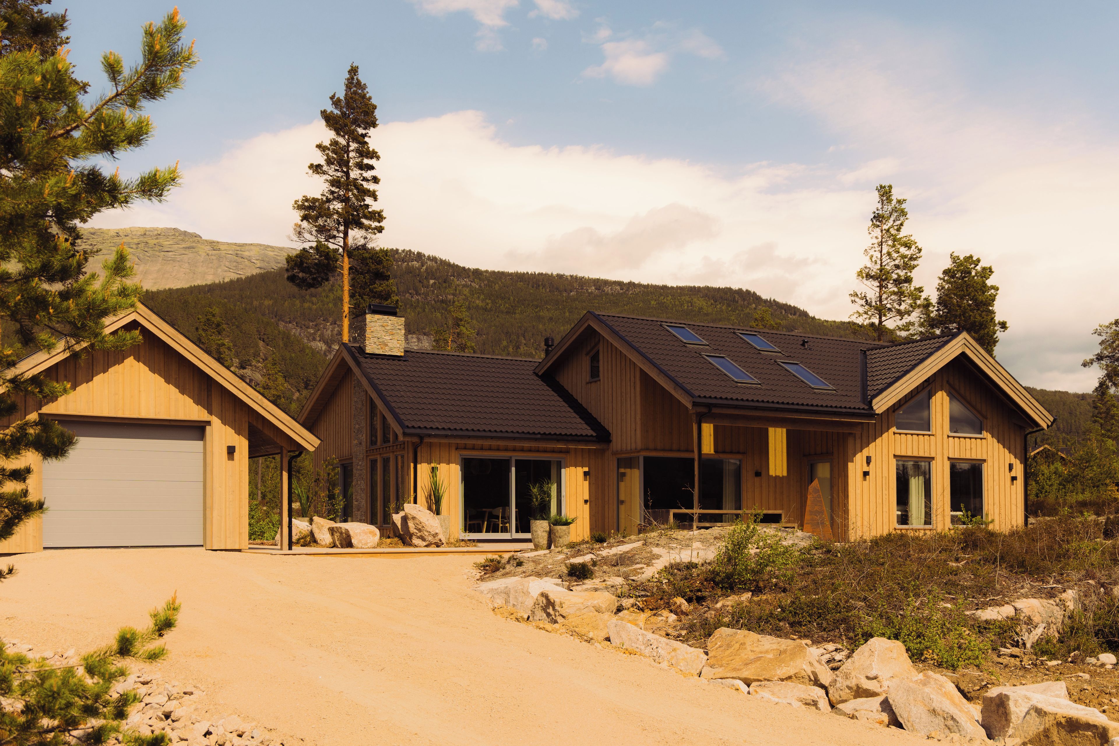 A modern two-story house with a large garage, a covered patio, and a mountain backdrop.