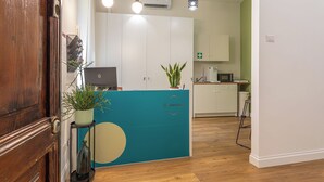 A reception area with a wooden door, a teal counter, potted plants, a laptop, and a white cabinet.