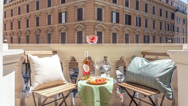 A balcony with a table set for two, featuring a bottle, glasses, and a plate of food.