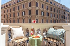 A balcony with a table set for two, featuring a bottle, glasses, and a plate of food. - Eufonia Vatican Golden Suites (Rome)