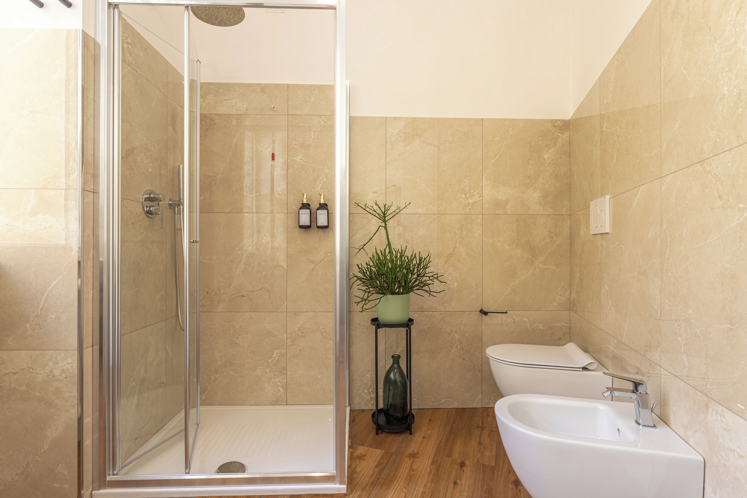 A modern bathroom with a glass shower enclosure, a white bathtub, a toilet, and a small potted plant on a shelf.