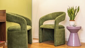 Two green armchairs, a small purple side table with a plant, and a wooden floor.
