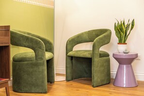 Dos sillones verdes, una mesita auxiliar morada con una planta y un suelo de madera.