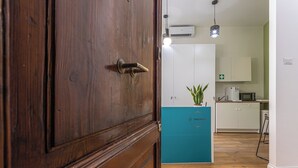A wooden door with a brass handle, a teal-colored counter with a plant, and a kitchen area with white cabinets and a microwave.