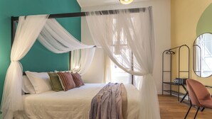 A bed with a canopy, pillows, a blanket, and a chair in a room with wooden flooring and a green wall.