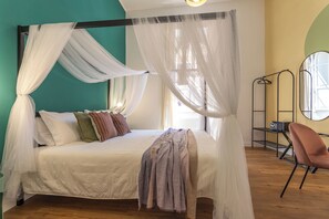 Una cama con dosel, almohadas, una manta y una silla en una habitación con piso de madera y pared verde.