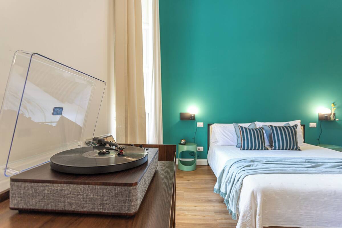 Habitación de hotel con cama, mesitas de noche, tocadiscos y una ventana con cortinas.