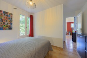 A bedroom with a bed, a window with curtains, a wall with a colorful artwork, and a hallway leading to another room. - Gîte de Maric: Among Olive Trees with Pool, Stunning Mountain Views (Aubres)