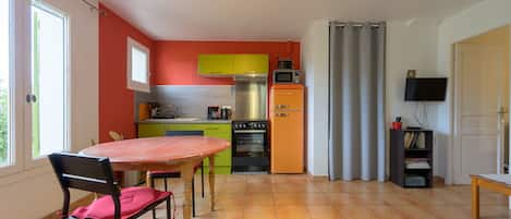 A compact kitchen with a dining area, a television, and a bookshelf.