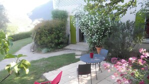 A patio with a table and chairs, surrounded by greenery and a building.