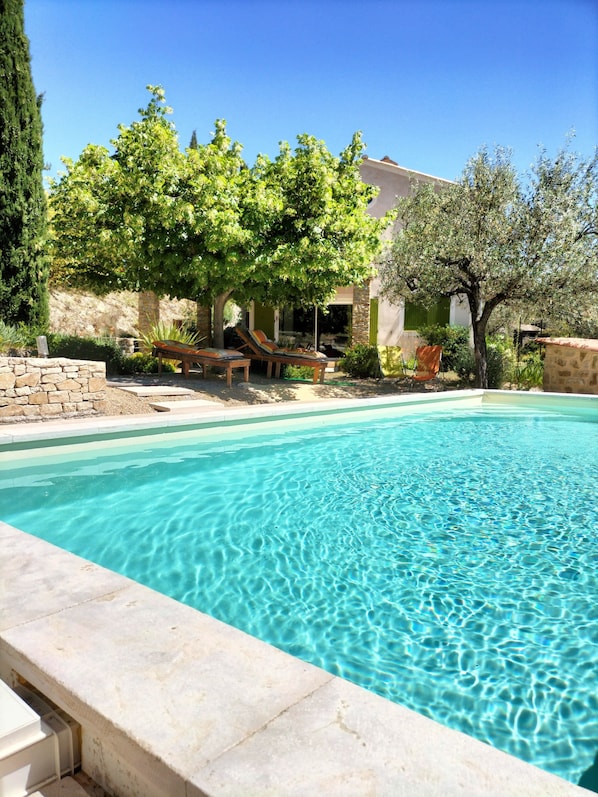 A clear swimming pool with lounge chairs and a stone wall.