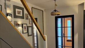 Eine Treppe mit Holzwandhandlauf, eine Wand mit gerahmten Bildern, eine Pendelleuchte und eine Tür zu einem Außenbereich.