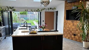 Eine moderne Küche mit Kochinsel, ein Essbereich mit einer Couch und ein an einer Holzwand montierter Fernseher.