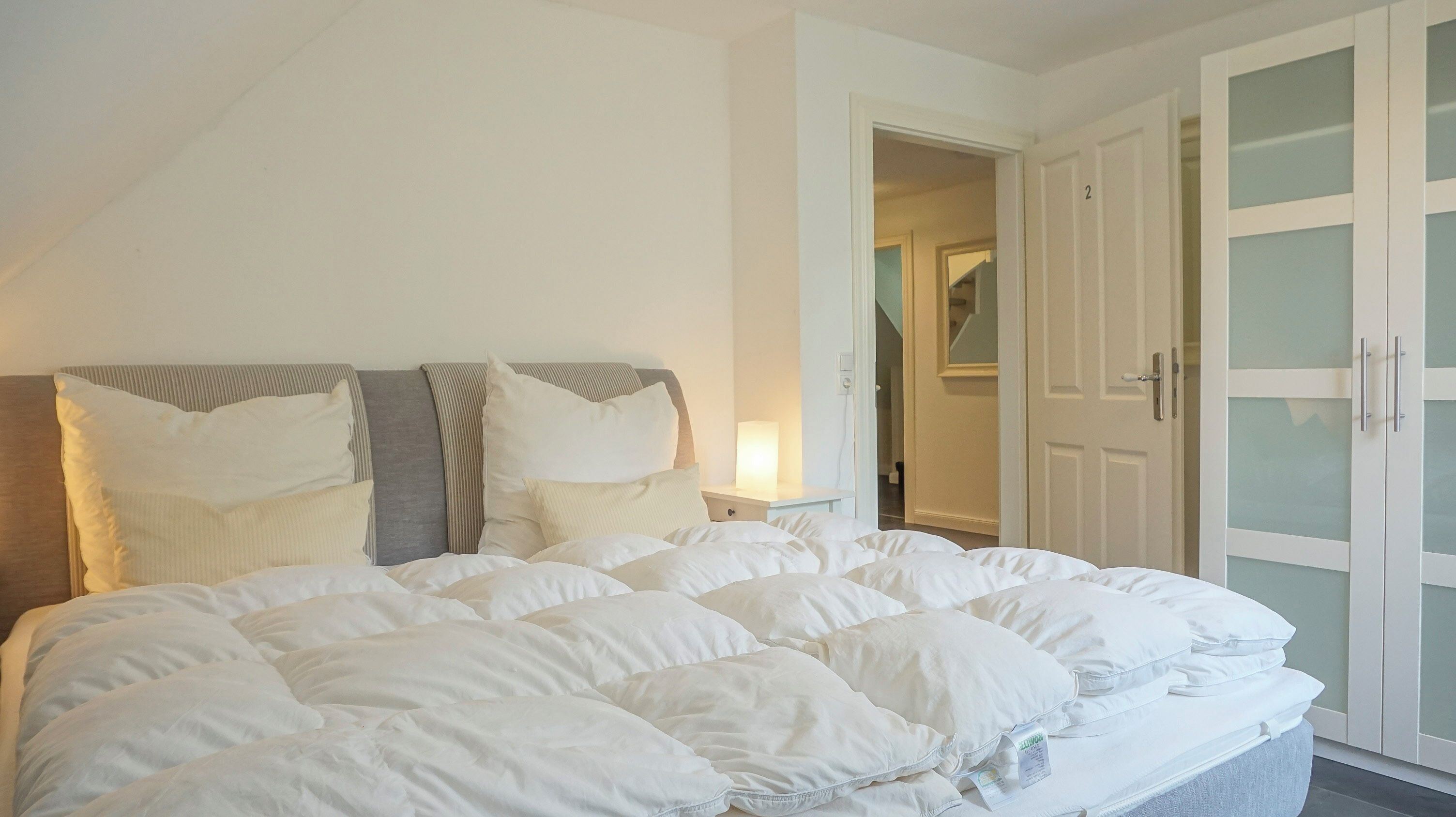 Ein Schlafzimmer mit einem großen Bett, einem Nachttisch mit Lampe und einem Kleiderschrank mit Milchglasschranktüren.