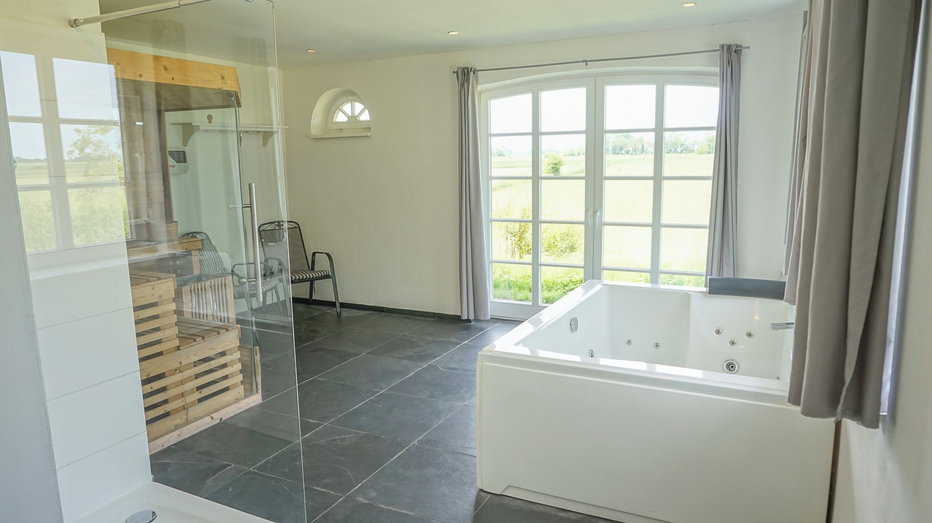 Ein modernes Badezimmer mit einer großen Badewanne, einer Duschkabine aus Glas und Blick ins Freie.