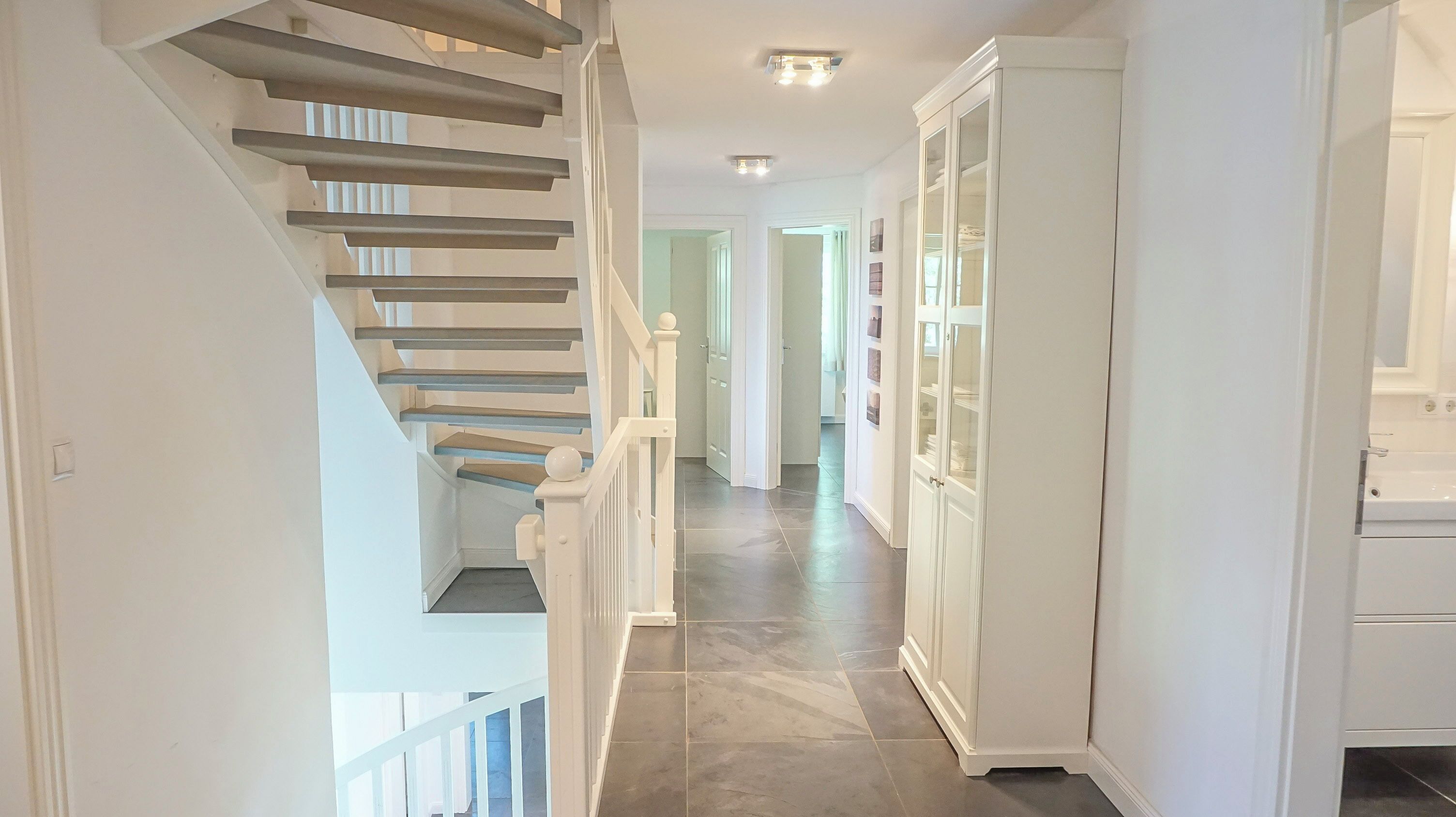 Eine Treppe mit weißen Geländern, ein Korridor mit einem weißen Schrank und ein Fliesenboden.