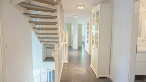A staircase with white railings, a hallway with a white cabinet, and a tiled floor. - Dünenwarft Süd: Thatched-roof house for 16 people (Tönning)