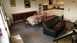 En matplats med ett bord, stolar och en svart lädersoffa. I bakgrunden finns ett kök med vita skåp och en kristallkrona.
