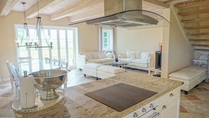 A modern kitchen with a large island, white furniture, and a high ceiling with exposed beams. - Warftkroog Thatched-Roof House: Thatched-roof house for 20 people with a sauna and hot tub (Katharinenheerd)