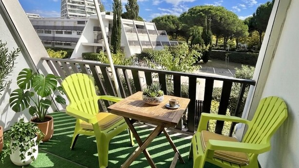 Ein Balkon mit Kunstgrasanlage, zwei grünen Stühlen, einem kleinen Tisch und Topfpflanzen.