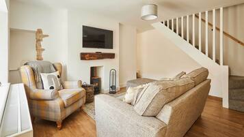 A living room with a sofa, armchair, fireplace, TV, and staircase.
