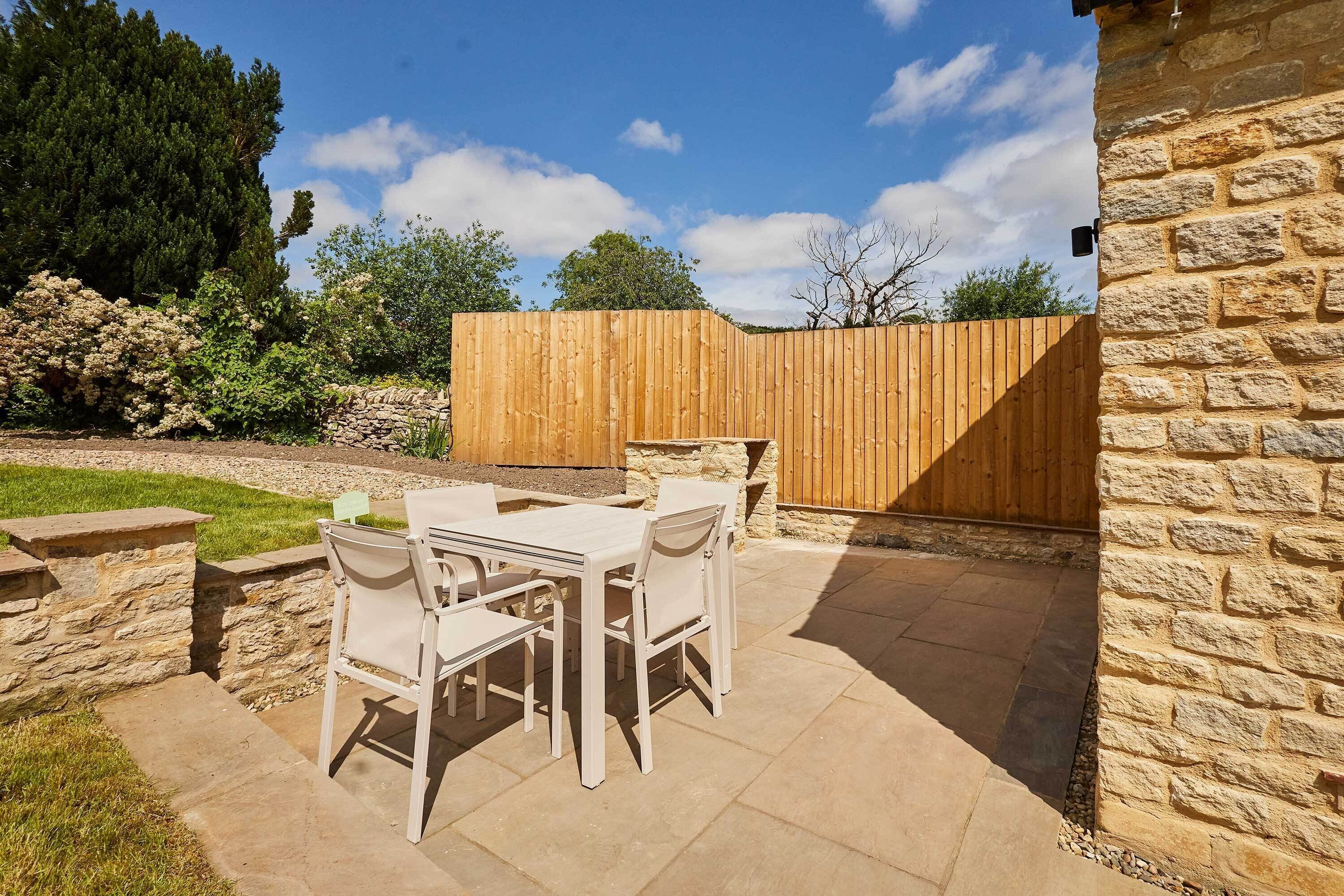 Une terrasse extérieure avec un mur en pierre, une clôture en bois et une table avec des chaises.