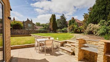 A patio with a stone barbecue, a table with chairs, and a stone wall.